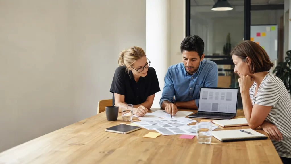 Website design brief writing — team reviewing website wireframes and planning notes at a meeting table